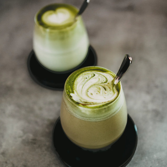 Zwei Gläser Matcha Tee auf einem grauem Untergrund.