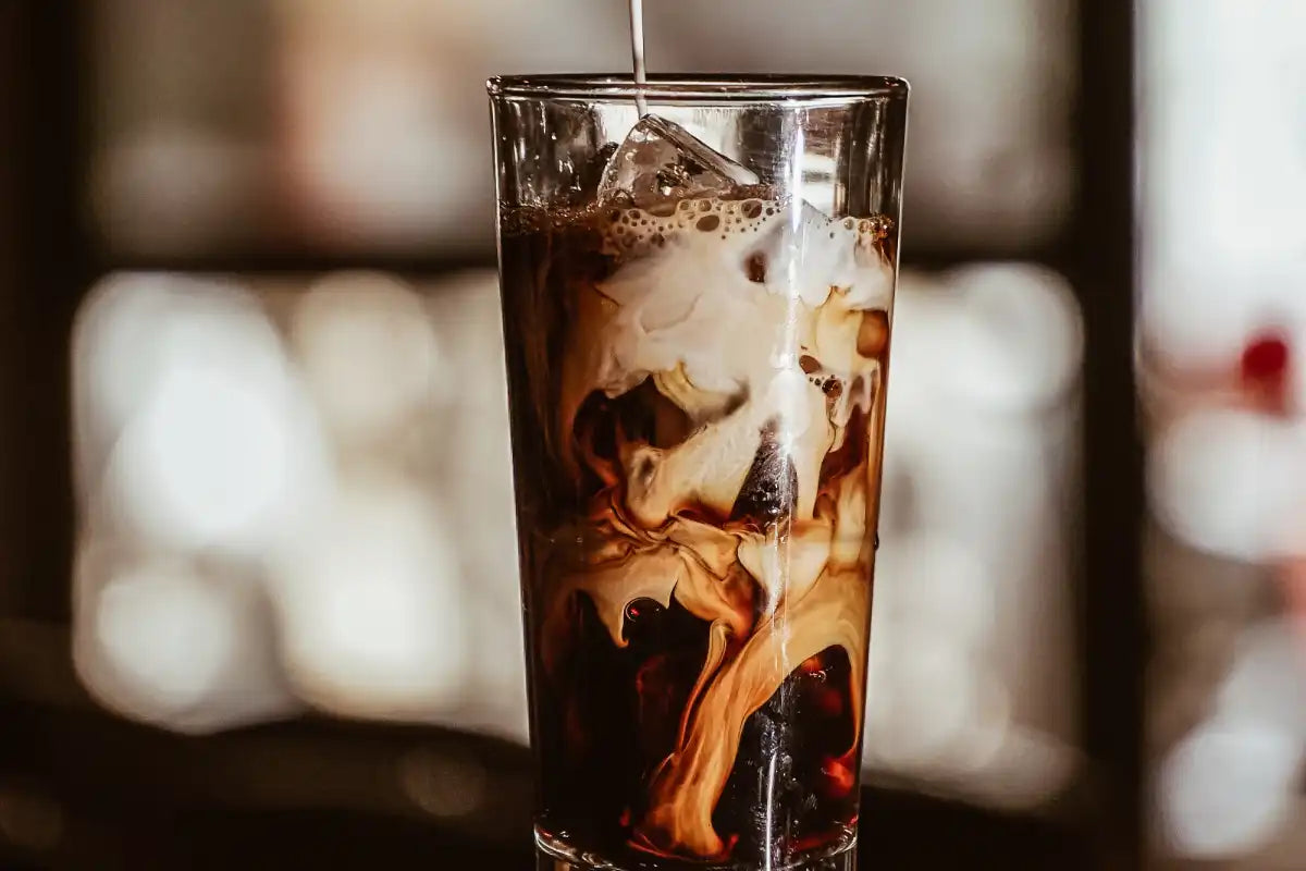 Ein Glas mit Cold Brew und Eis in das Milch geschüttet wird 
