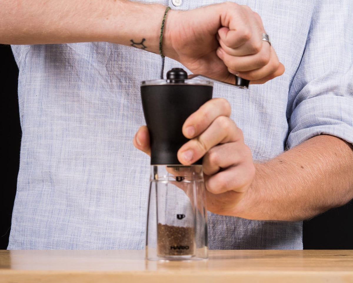 Eine Person mahlt per Hand Kaffee mit einer Kaffeemühle.