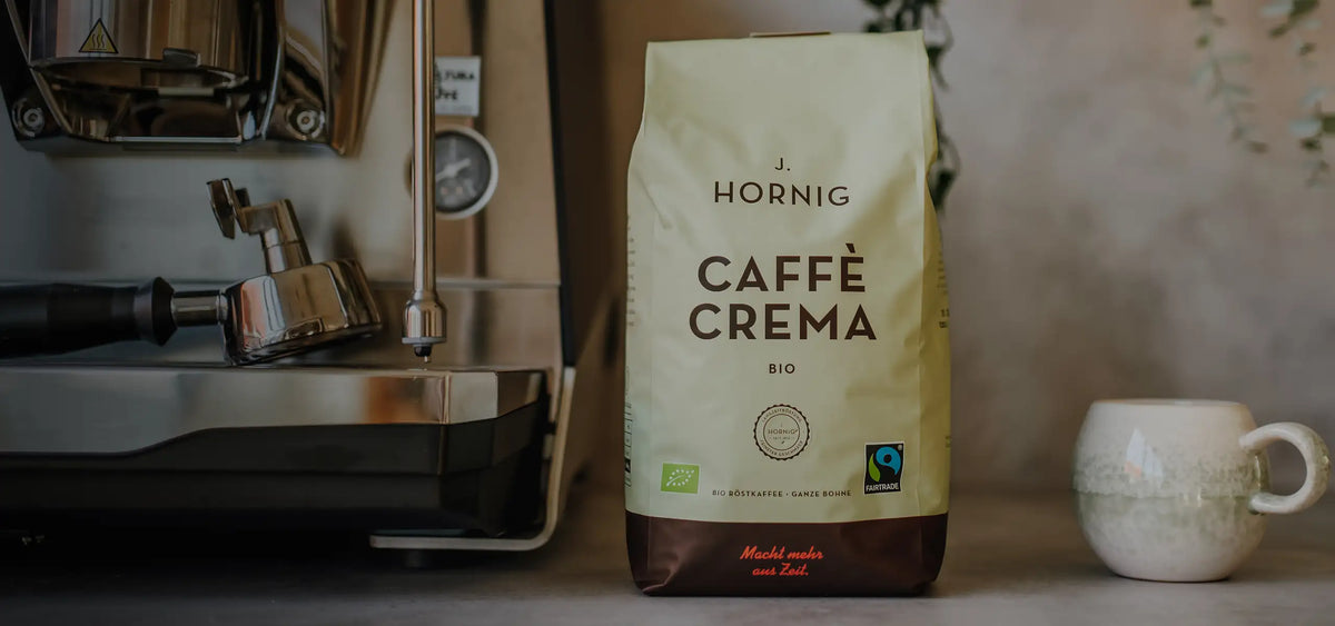 Eine Packung J. Hornig Caffe Crema Bio neben einer Siebträgermaschine und einer Kaffeetasse