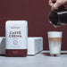 Eine Packung J. Hornig Caffe Crema Classico mit einem Latte Machiato Glas und einer Kanne auf weißem Untergrund mit braunem Hintergrund
