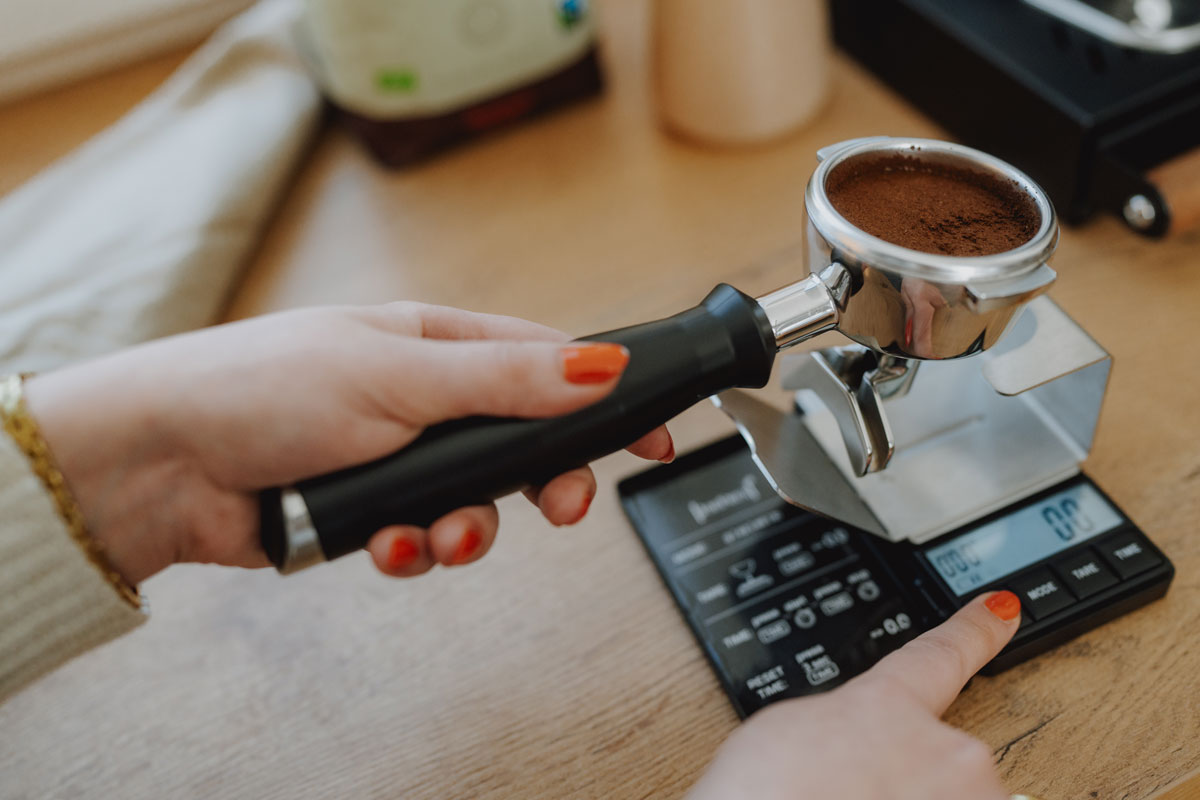 Frau haltet Siebträger in der Hand und betätigt Espresso-Waage von JoeFrex, welche im J. Hornig Onlineshop erhältlich ist.