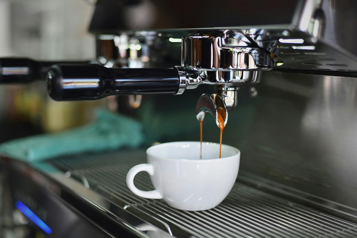 Siebträgermaschine und Kaffeetasse in welche gerade Kaffee fließt