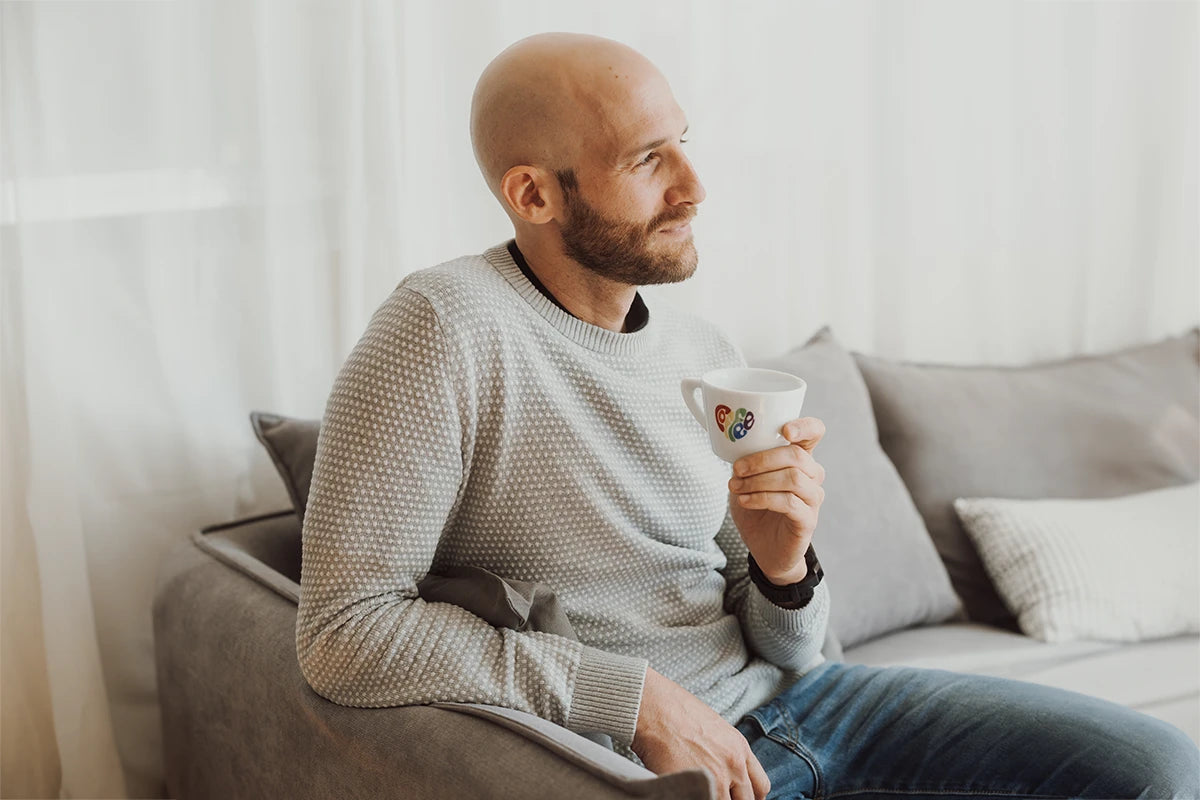 Junger Mann sitzt auf einem Sofa und hält eine J. Hornig Pride Tassen 2024 in der Hand