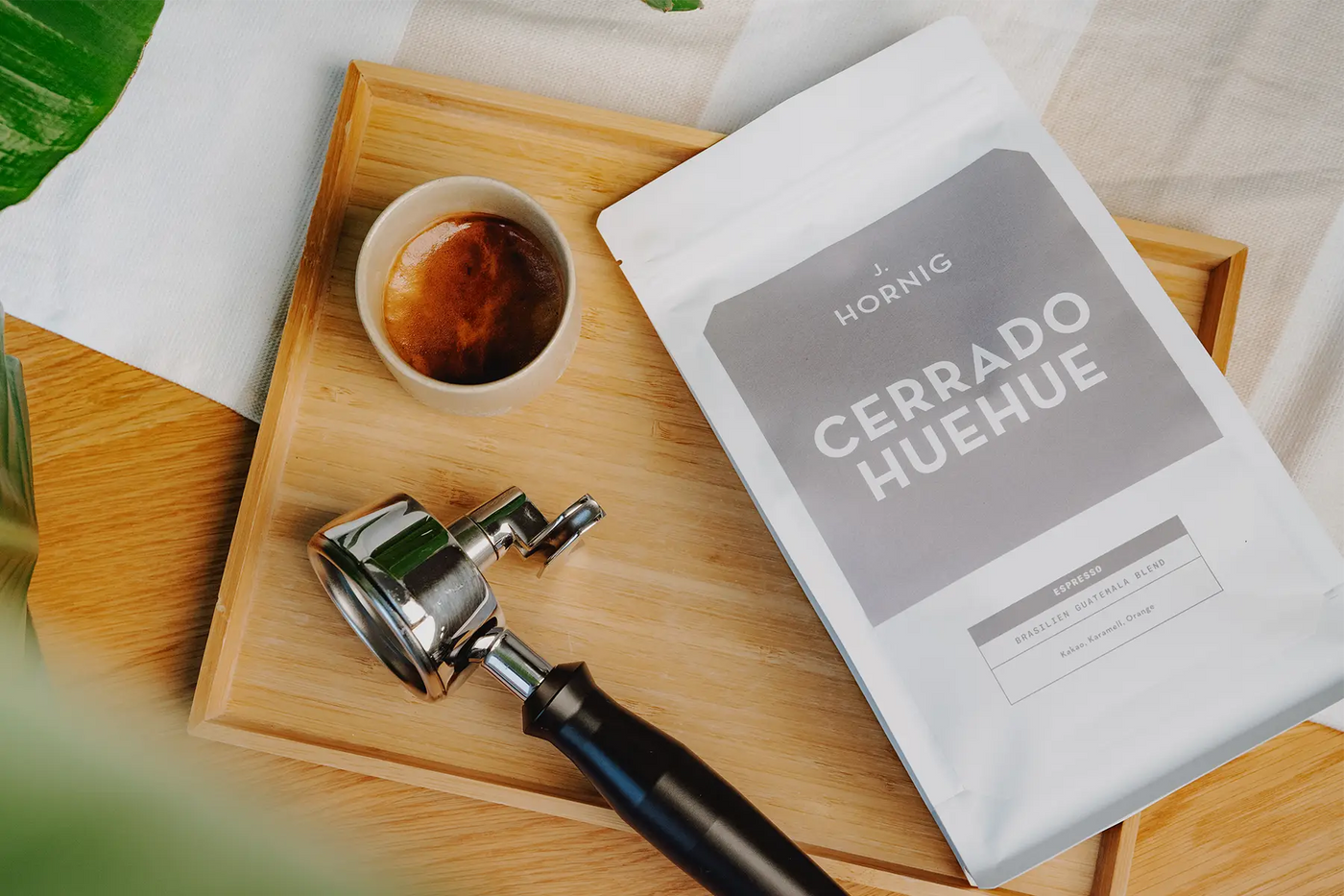 Eine Packung J. Hornig Spezialitätenkaffee Cerrado Huehue Espresso auf einem Holztablett mit einem Siebträger und einer Tasse Kaffee
