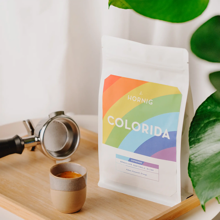 Eine Packungen J. Hornig Spezialitätenkaffee Colorida Espresso  Brasilien Guatemala Blend auf Holzbrett mit einem Espresso und einem Siebträger.