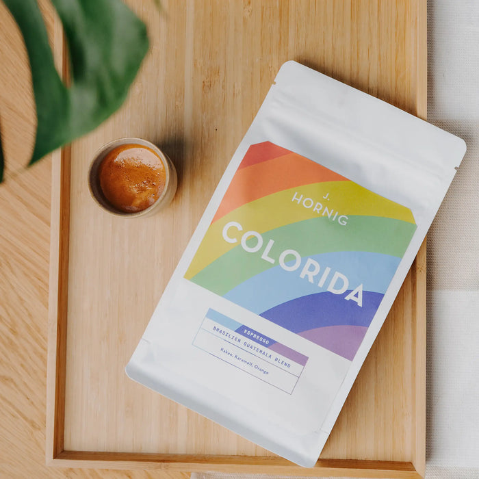 Eine Packung J. Hornig Spezialitätenkaffee Colorida Espresso Limited Edition Brasilien Guatemala Blend liegend auf einem Holztisch mit einer Tasse Espresso