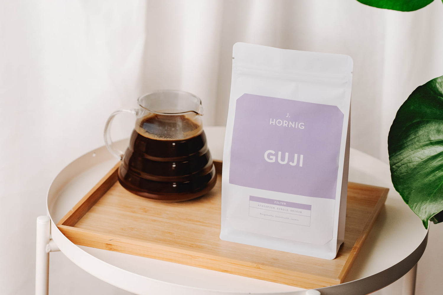 J. Hornig Guji Spezialitätenkaffee auf einem Tablett mit Glaskanne Filterkaffee und Zimmerpflanze im Hintergrund.