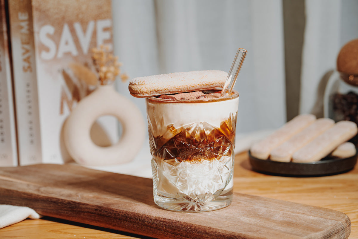 Ein Glas gefüllt mit Tiramisu Iced Latte auf einem Holzbrett, gemacht mit J. Hornig Kaffee.