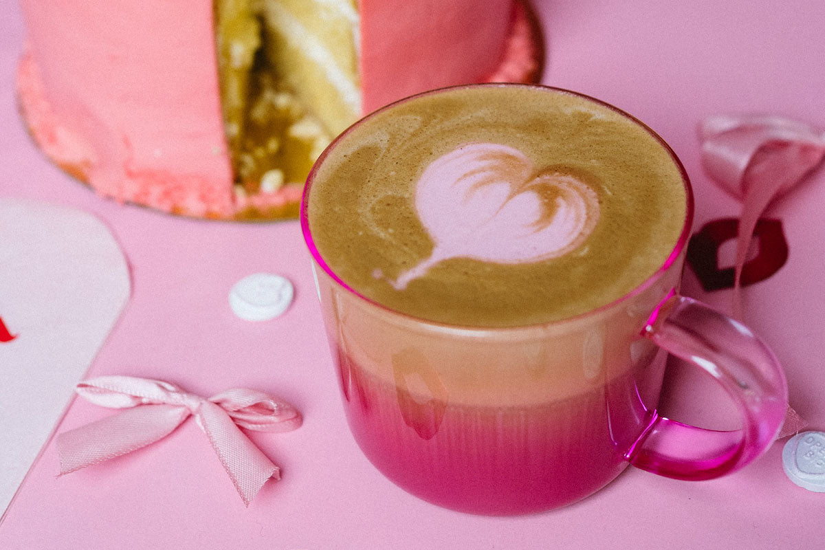 Man sieht auf einem Tisch einen pinken Cappuccino, in einer pinken Tasse.